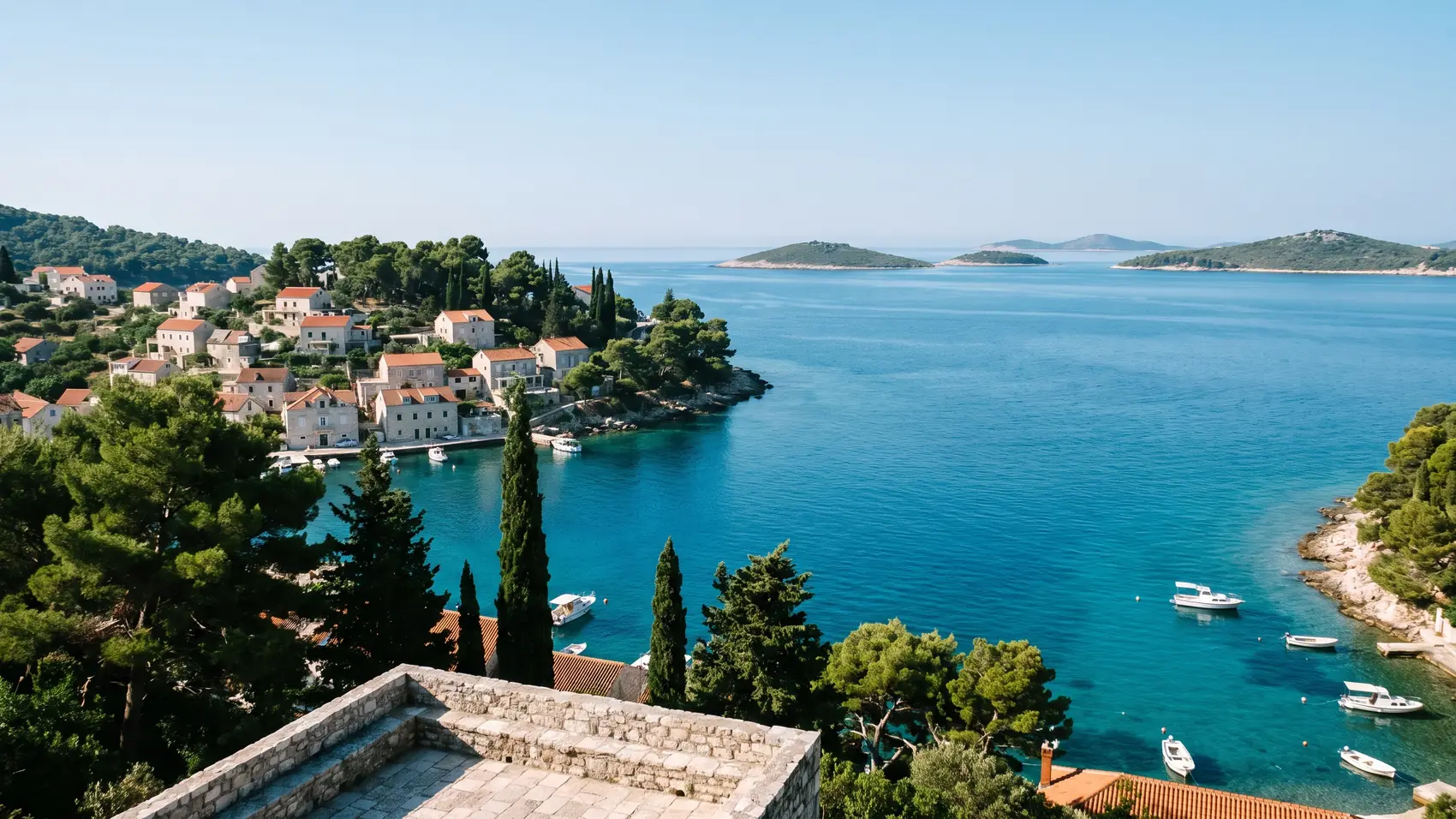 A bay with stone houses, pines and small boats, seen from above